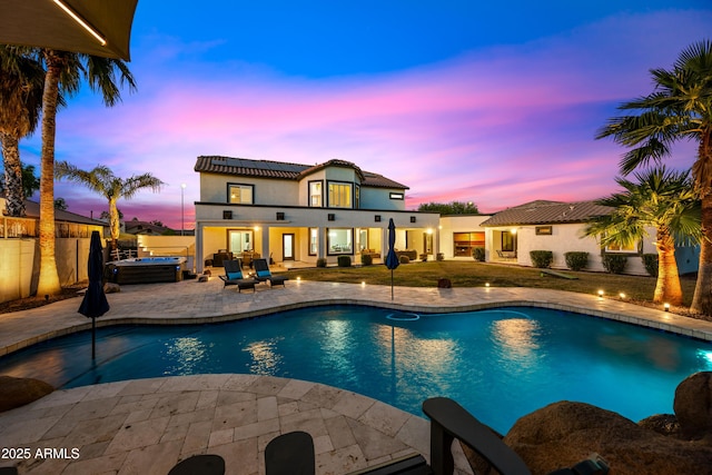 pool at dusk with a patio and a hot tub