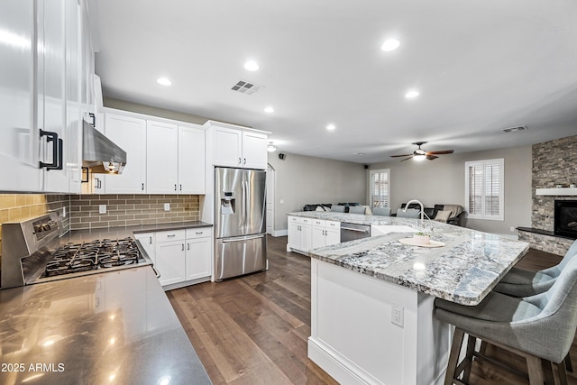 kitchen featuring white cabinetry, stainless steel appliances, a kitchen breakfast bar, light stone counters, and range hood