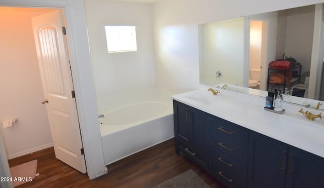 bathroom featuring tiled bath, vanity, hardwood / wood-style flooring, and toilet