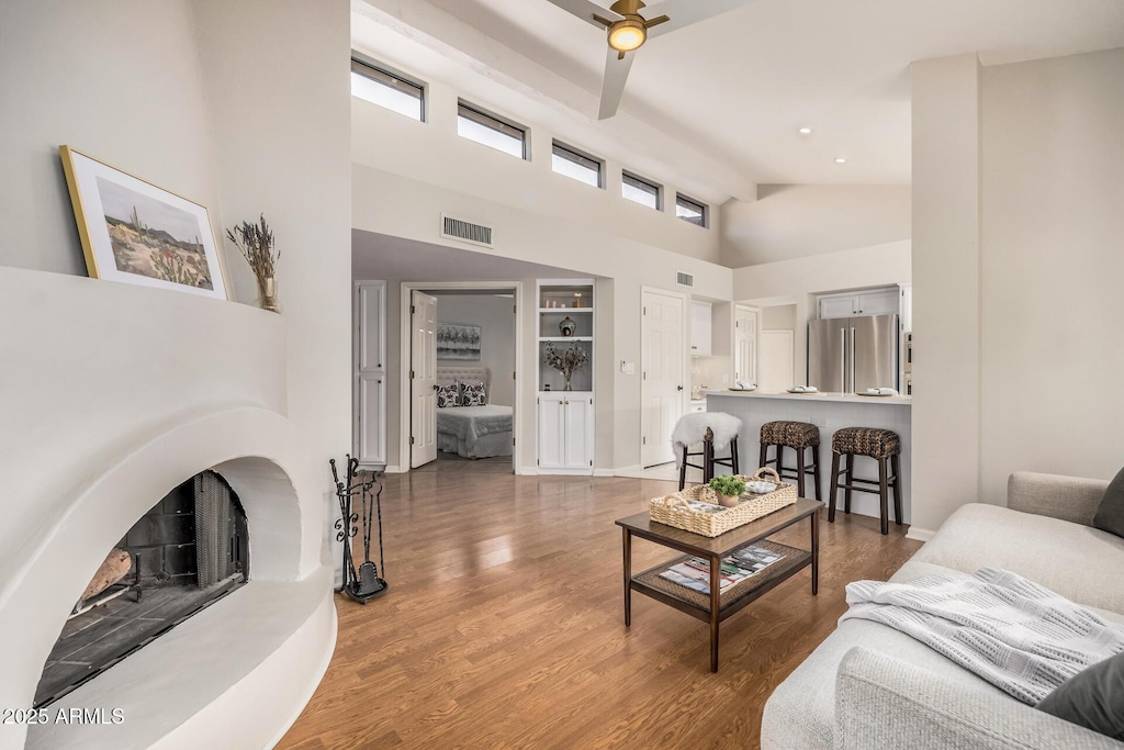 living room with hardwood / wood-style flooring, ceiling fan, a high ceiling, and built in shelves