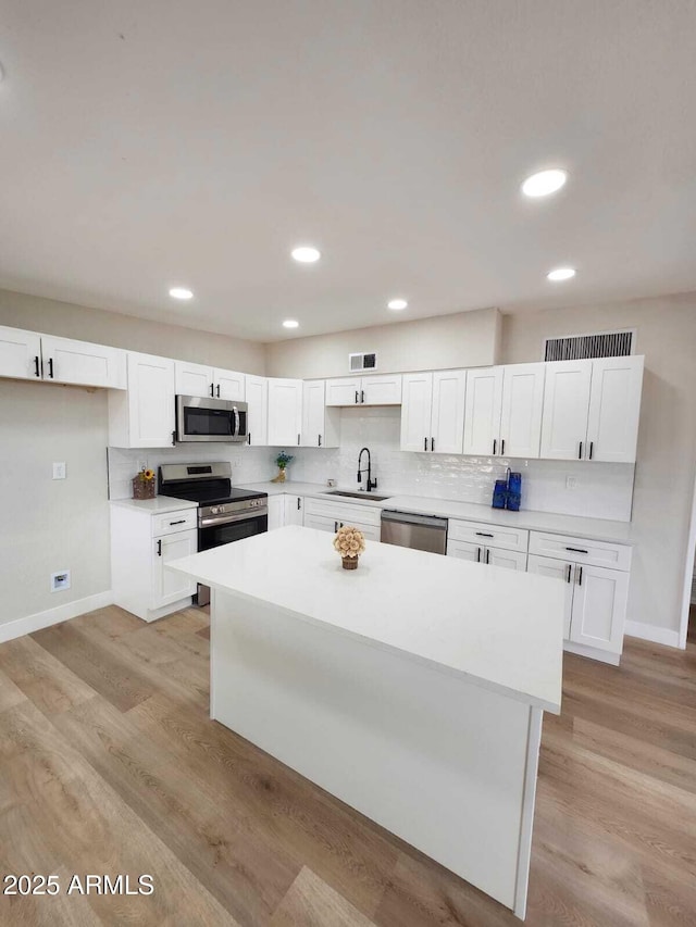 kitchen featuring appliances with stainless steel finishes, white cabinetry, sink, decorative backsplash, and light hardwood / wood-style flooring