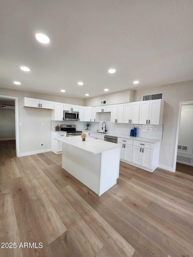 kitchen with appliances with stainless steel finishes, sink, white cabinets, and light hardwood / wood-style floors