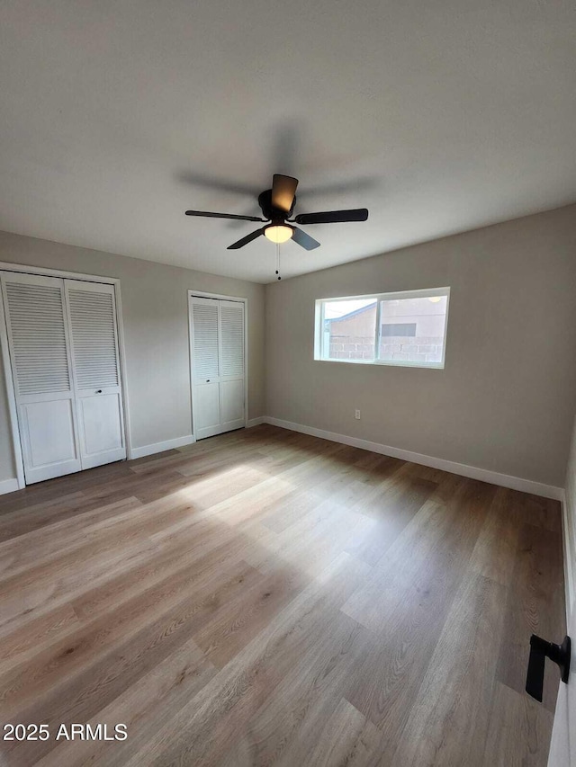 unfurnished bedroom with multiple closets, ceiling fan, and light hardwood / wood-style floors