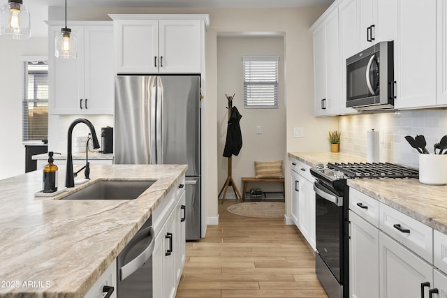 kitchen featuring pendant lighting, sink, light stone countertops, appliances with stainless steel finishes, and white cabinets