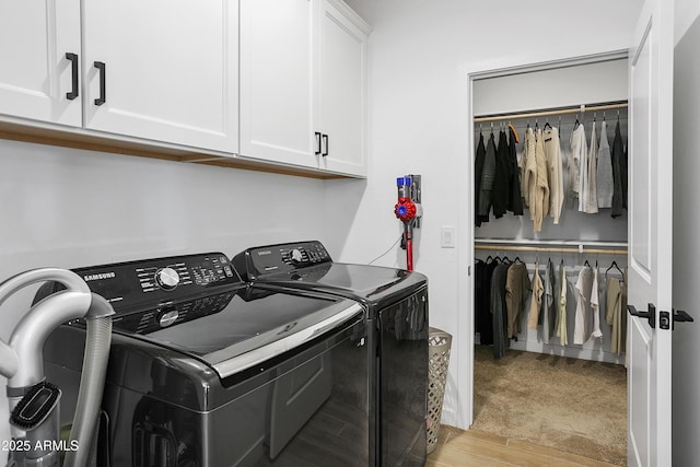 clothes washing area with washer and dryer, light hardwood / wood-style floors, and cabinets