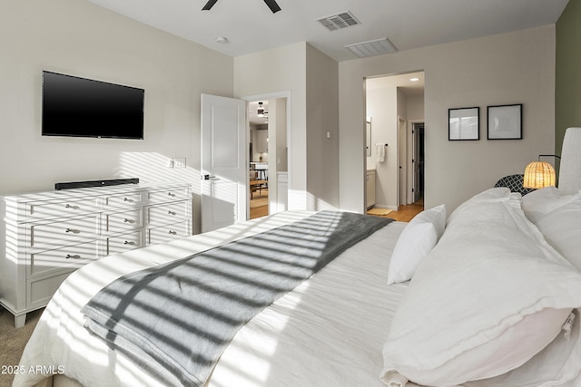 bedroom with ceiling fan, light colored carpet, and ensuite bathroom