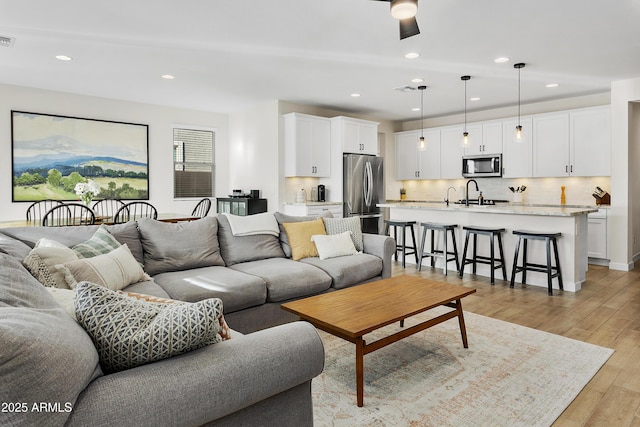 living room with ceiling fan, sink, and light hardwood / wood-style flooring