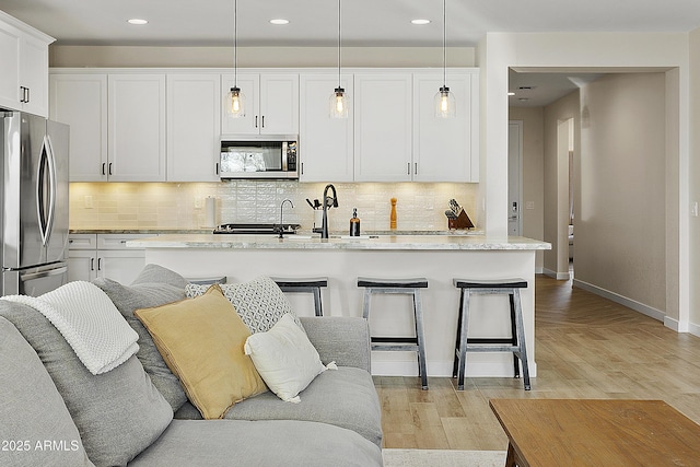 kitchen with stainless steel appliances, an island with sink, white cabinetry, and decorative light fixtures