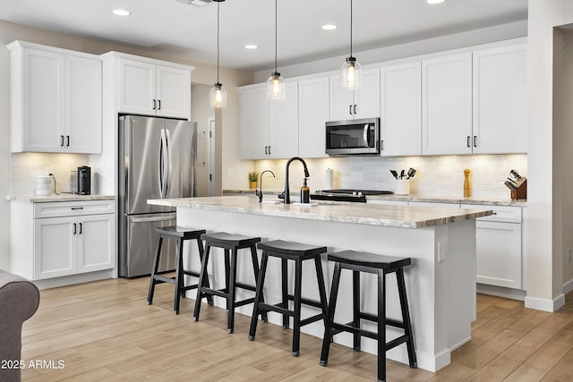 kitchen featuring a center island with sink, stainless steel appliances, pendant lighting, and white cabinetry