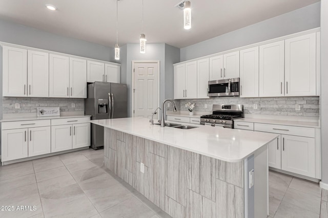 kitchen featuring a center island with sink, light countertops, a sink, appliances with stainless steel finishes, and backsplash