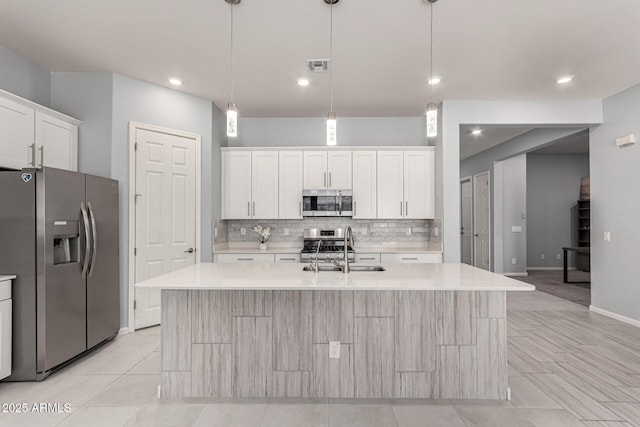 kitchen with decorative backsplash, appliances with stainless steel finishes, a sink, light countertops, and white cabinetry