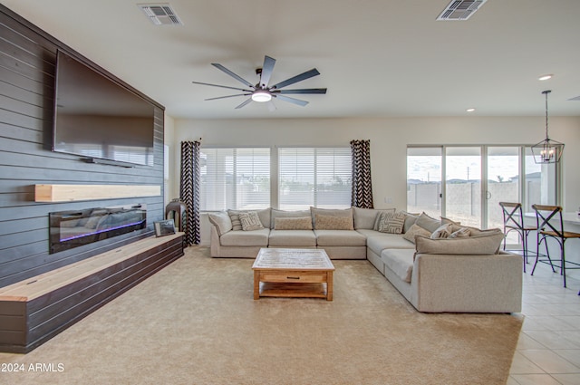 living room with a fireplace, light tile patterned flooring, ceiling fan with notable chandelier, and wooden walls