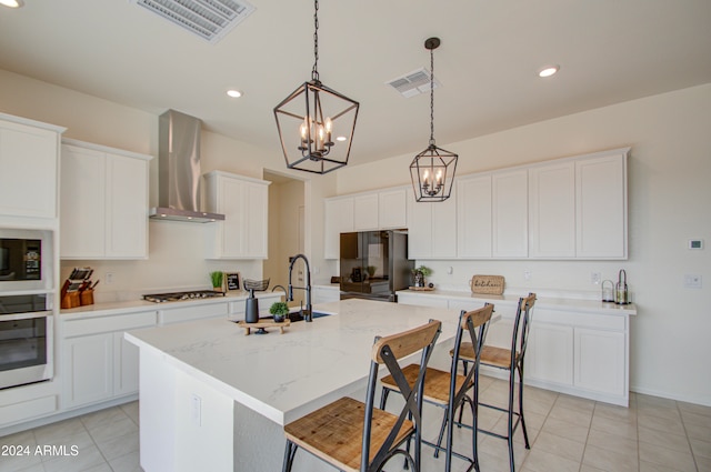 kitchen with stainless steel appliances, sink, a kitchen island with sink, wall chimney range hood, and white cabinetry