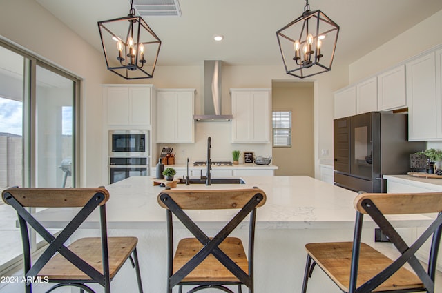 kitchen with white cabinetry, wall chimney range hood, decorative light fixtures, and an island with sink