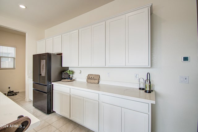 kitchen featuring white cabinetry, black fridge, light stone countertops, and light tile patterned flooring