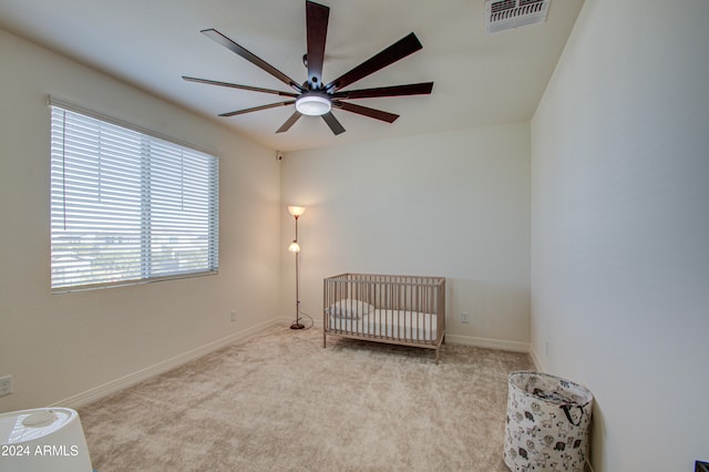 carpeted bedroom featuring a crib and ceiling fan