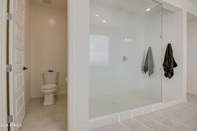 bathroom with toilet, tiled shower, and tile patterned floors