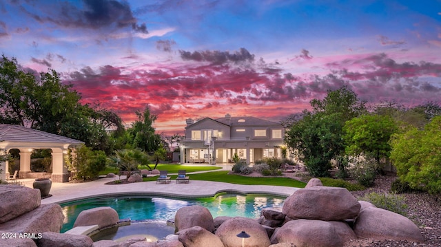 pool at dusk with an in ground hot tub, a patio, and a lawn