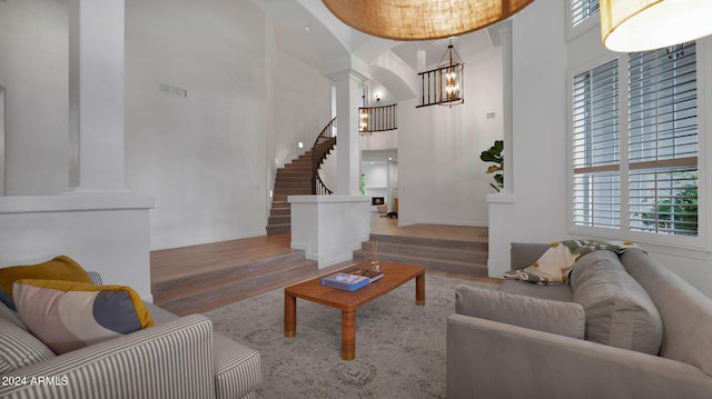 living room featuring hardwood / wood-style floors, decorative columns, a chandelier, and a towering ceiling