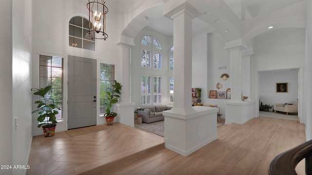 entryway featuring a high ceiling, light parquet floors, ornate columns, and a chandelier