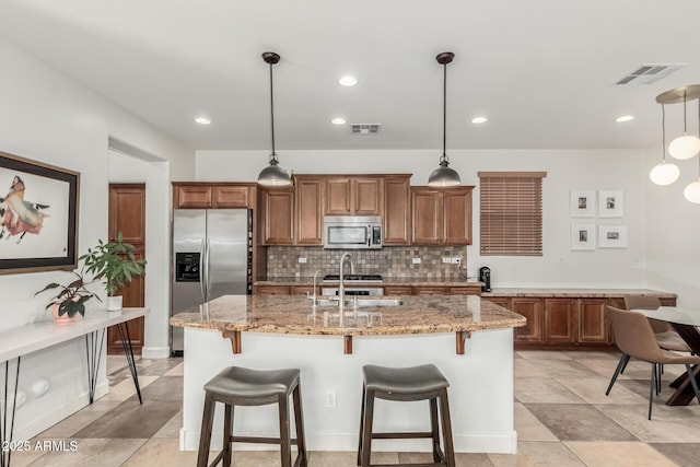 kitchen with decorative light fixtures, an island with sink, appliances with stainless steel finishes, and tasteful backsplash