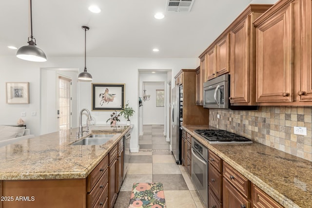 kitchen featuring pendant lighting, sink, light tile patterned flooring, appliances with stainless steel finishes, and an island with sink