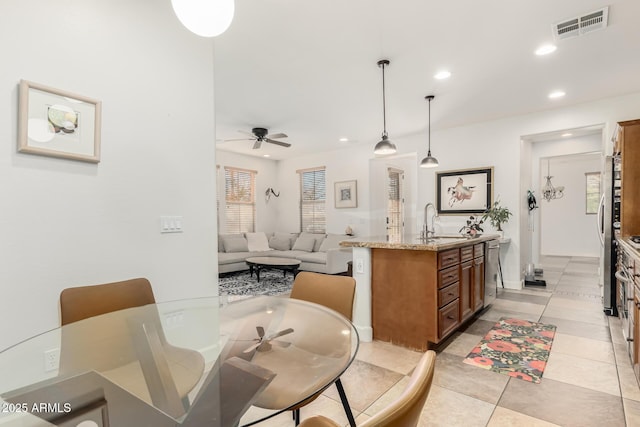 kitchen with light stone countertops, pendant lighting, an island with sink, sink, and light tile patterned flooring