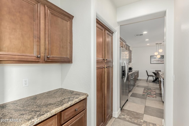 kitchen with stone counters, stainless steel fridge, and decorative light fixtures