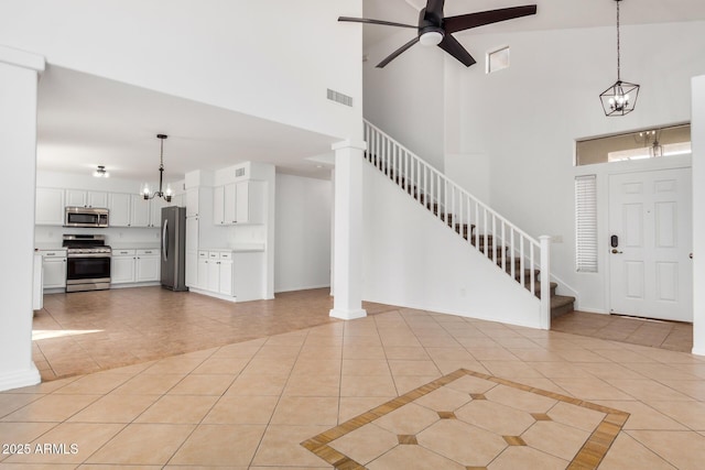 foyer with stairway, visible vents, baseboards, light tile patterned flooring, and ceiling fan with notable chandelier