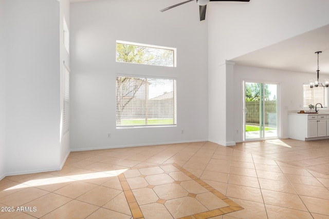 unfurnished room with baseboards, light tile patterned floors, ceiling fan with notable chandelier, a towering ceiling, and a sink