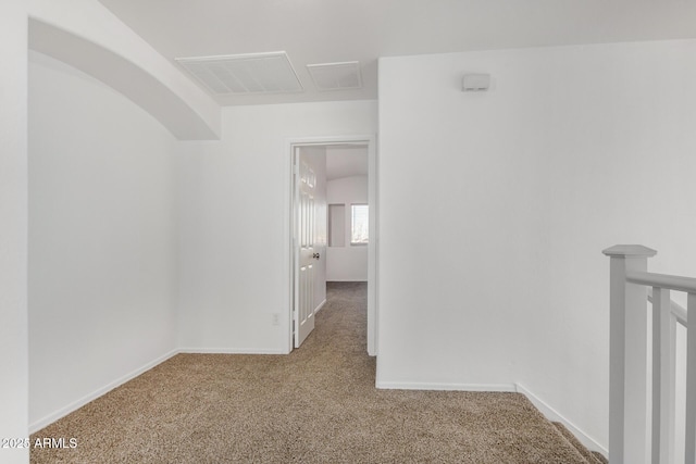 carpeted empty room with visible vents, baseboards, and arched walkways