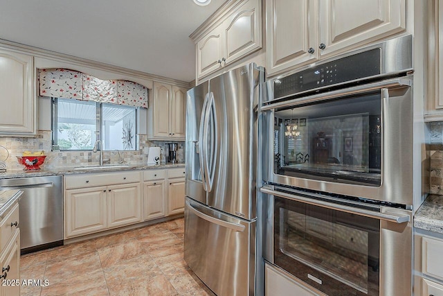 kitchen featuring light stone counters, cream cabinets, stainless steel appliances, a sink, and tasteful backsplash