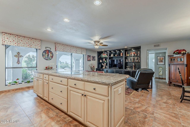 kitchen with a kitchen island, a ceiling fan, visible vents, cream cabinetry, and white electric cooktop