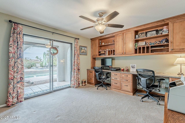 carpeted office space featuring ceiling fan and built in desk