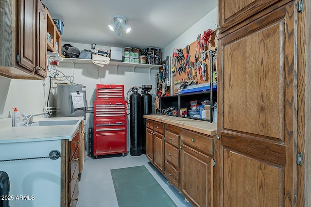 kitchen with finished concrete flooring, open shelves, light countertops, brown cabinetry, and electric water heater