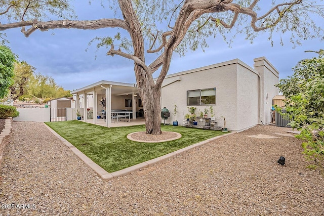 rear view of house featuring fence, a yard, a gate, stucco siding, and a patio area