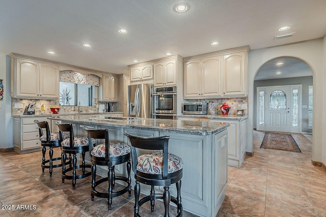 kitchen with arched walkways, a breakfast bar area, visible vents, appliances with stainless steel finishes, and a kitchen island