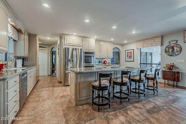 kitchen with arched walkways, a breakfast bar, stainless steel appliances, a sink, and a kitchen island