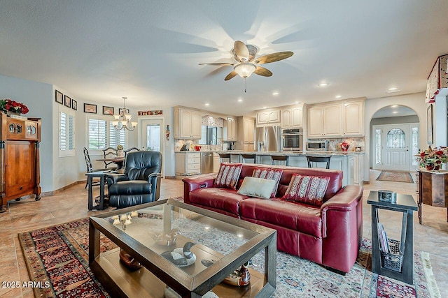 living area featuring arched walkways, baseboards, recessed lighting, and ceiling fan with notable chandelier