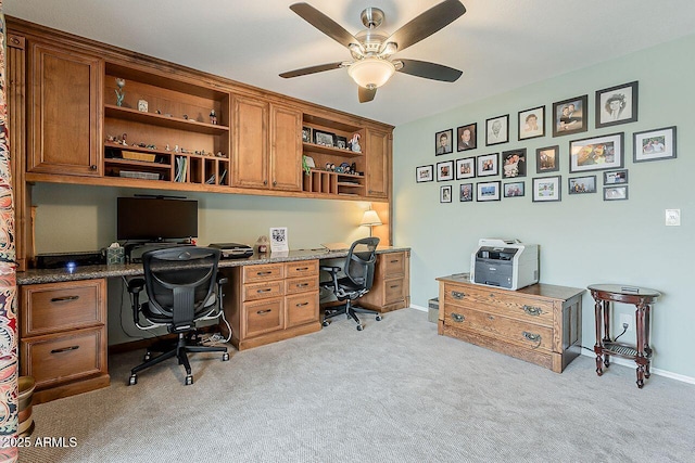 office space with built in study area, ceiling fan, light carpet, and baseboards