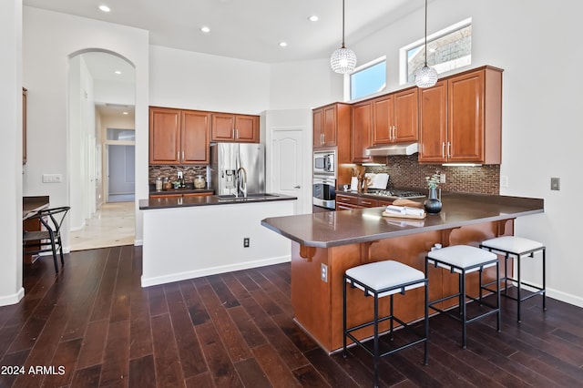 kitchen with kitchen peninsula, dark wood-type flooring, pendant lighting, and appliances with stainless steel finishes