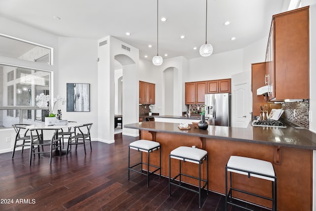 kitchen with a high ceiling, dark hardwood / wood-style flooring, stainless steel refrigerator with ice dispenser, decorative light fixtures, and decorative backsplash