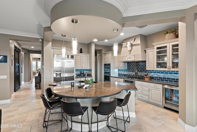 kitchen with pendant lighting, appliances with stainless steel finishes, wine cooler, an island with sink, and custom exhaust hood