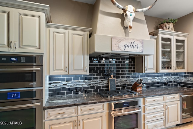 kitchen featuring cream cabinetry, custom range hood, beverage cooler, and appliances with stainless steel finishes