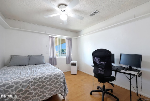 bedroom with ceiling fan, light hardwood / wood-style floors, and a textured ceiling