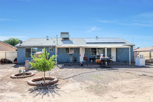 rear view of house with solar panels, cooling unit, a patio area, and a fire pit