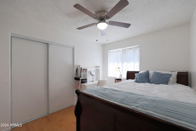 bedroom with light wood-type flooring, a textured ceiling, ceiling fan, and a closet