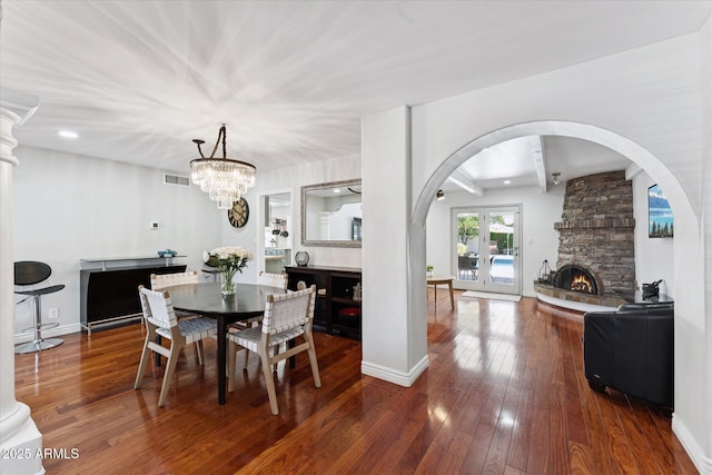 7835 E Cannon Dr, Scottsdale, AZ 85258 - dining space featuring arched walkways, a stone fireplace, wood-type flooring, beam ceiling, and a chandelier