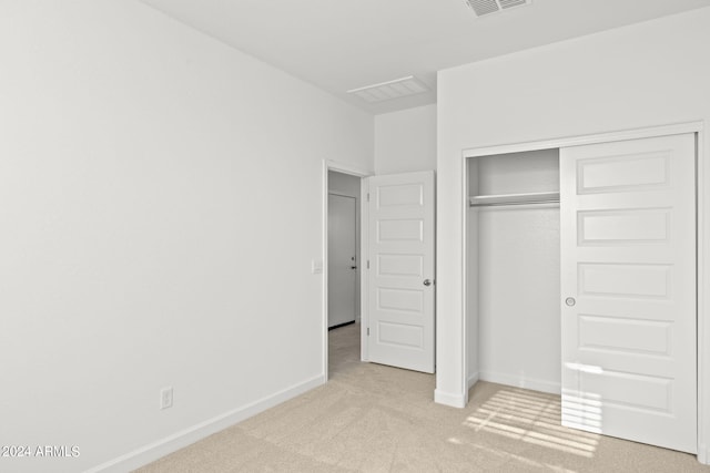 unfurnished bedroom with light colored carpet and a closet