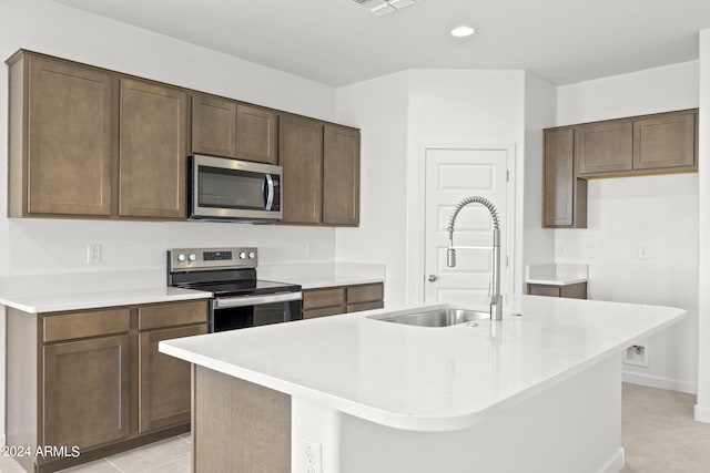 kitchen featuring sink, an island with sink, light tile patterned floors, and appliances with stainless steel finishes